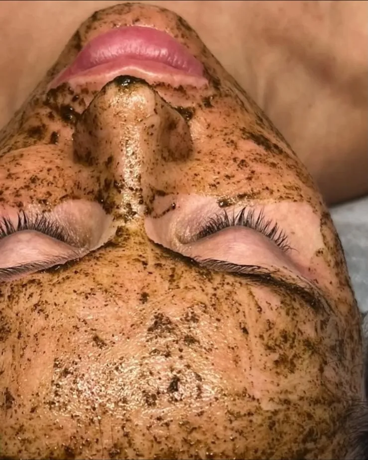 A client lying back with the dark BioPhyto herbal peel applied over her face, eyes closed