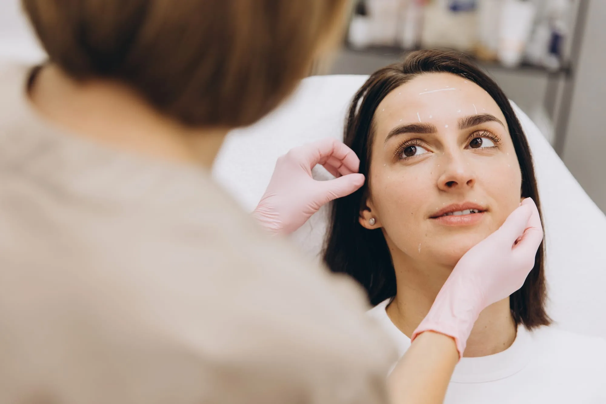 A practitioner in pink gloves checking a client’s face before a treatment