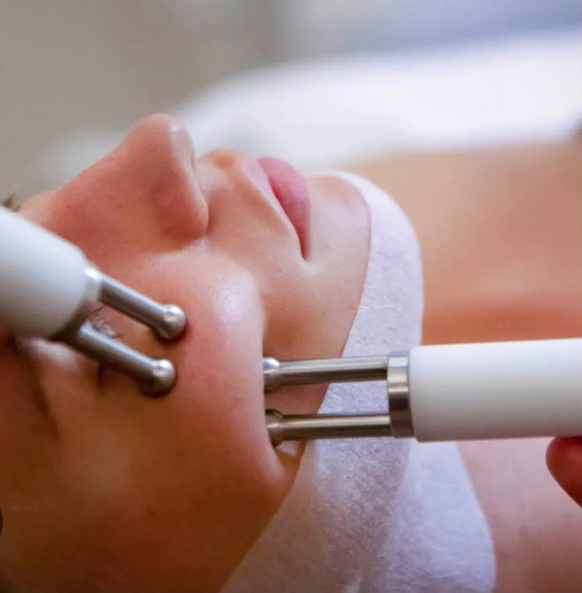 Two metal microcurrent probes lifting the skin along a client’s cheek and jaw