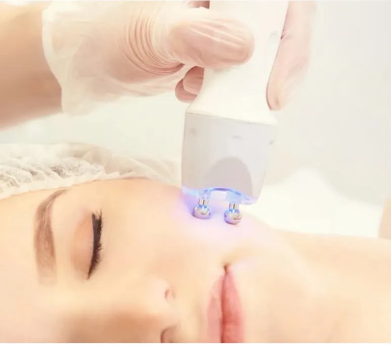 A white handpiece with two glowing electrodes on a client’s cheek during an EMS treatment