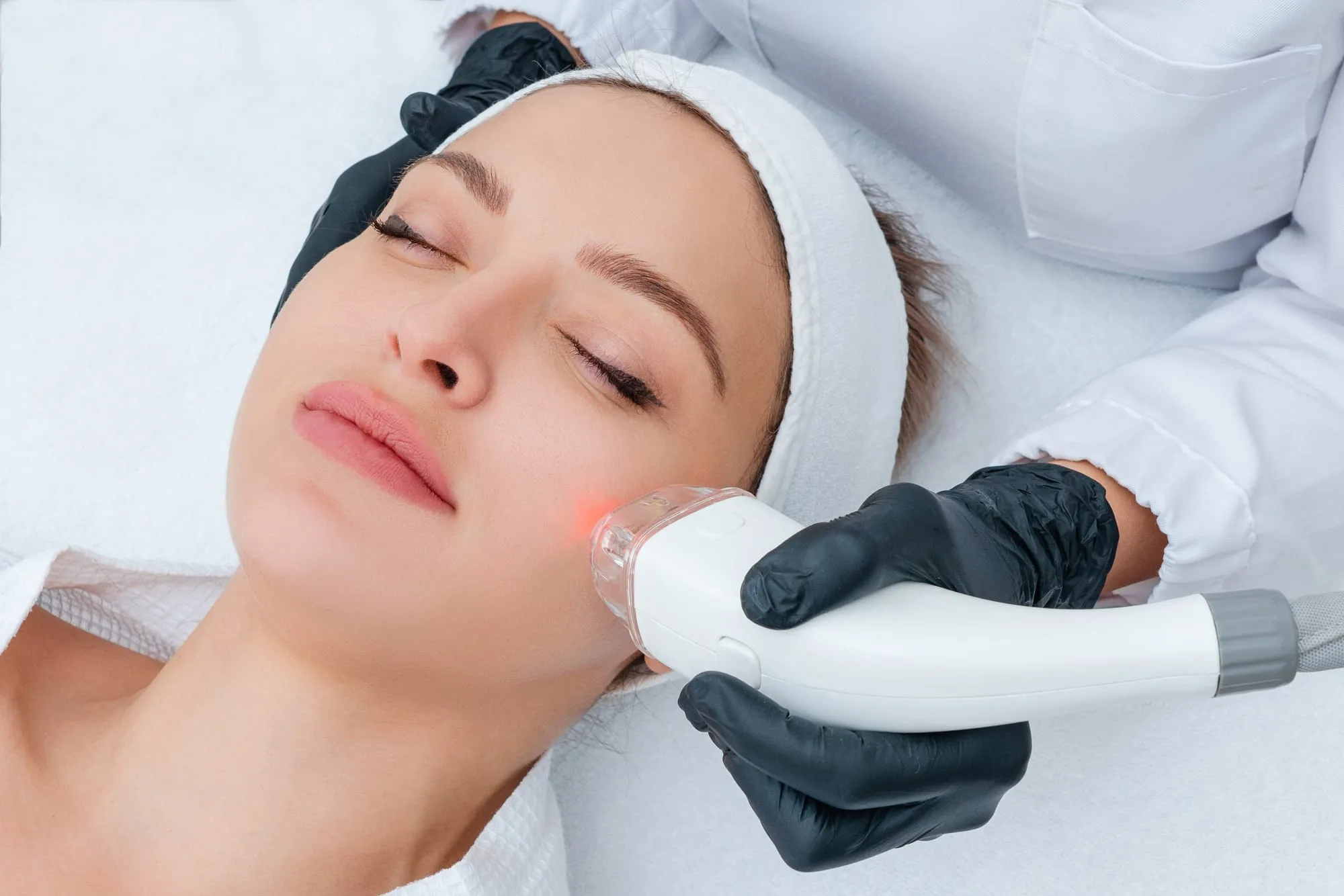 A client with closed eyes while a handpiece moves over her cheek
